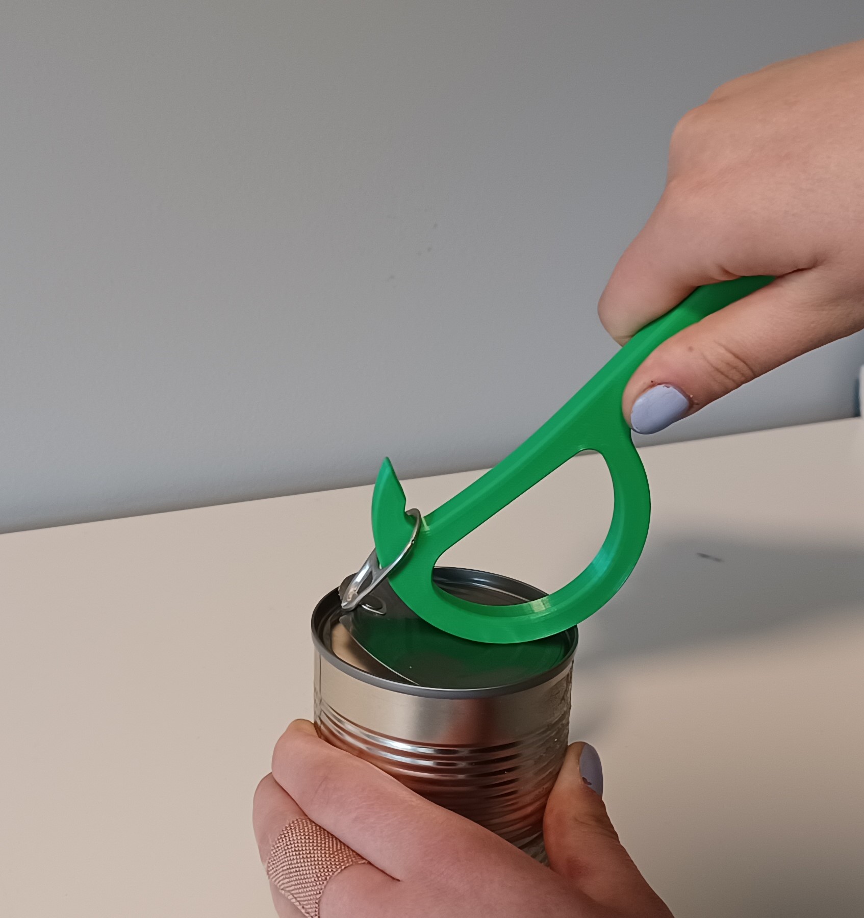 A person using a Pull-Tab Tin Can Opener to open an aluminum can.