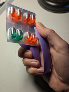 A person using a Blister Pack Opener to open a blister pack of pills.