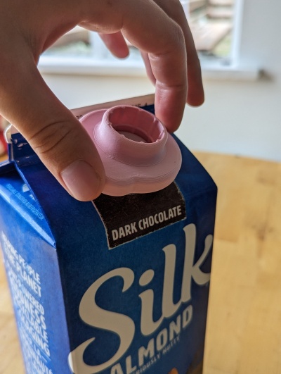 A person using a Milk Carton Opener on a carton of dark chocolate soy milk.