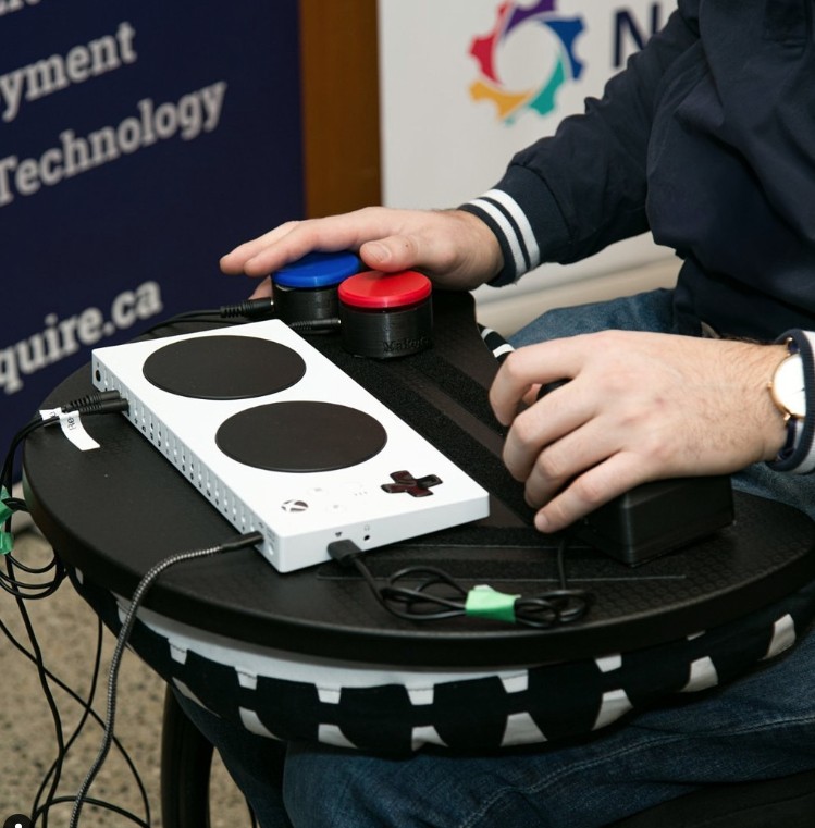 A person uses an Xbox Adaptive Controller and switches on a lap tray to play a video game.