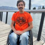 William, who is in a wheelchair, wears an orange shirt with text 