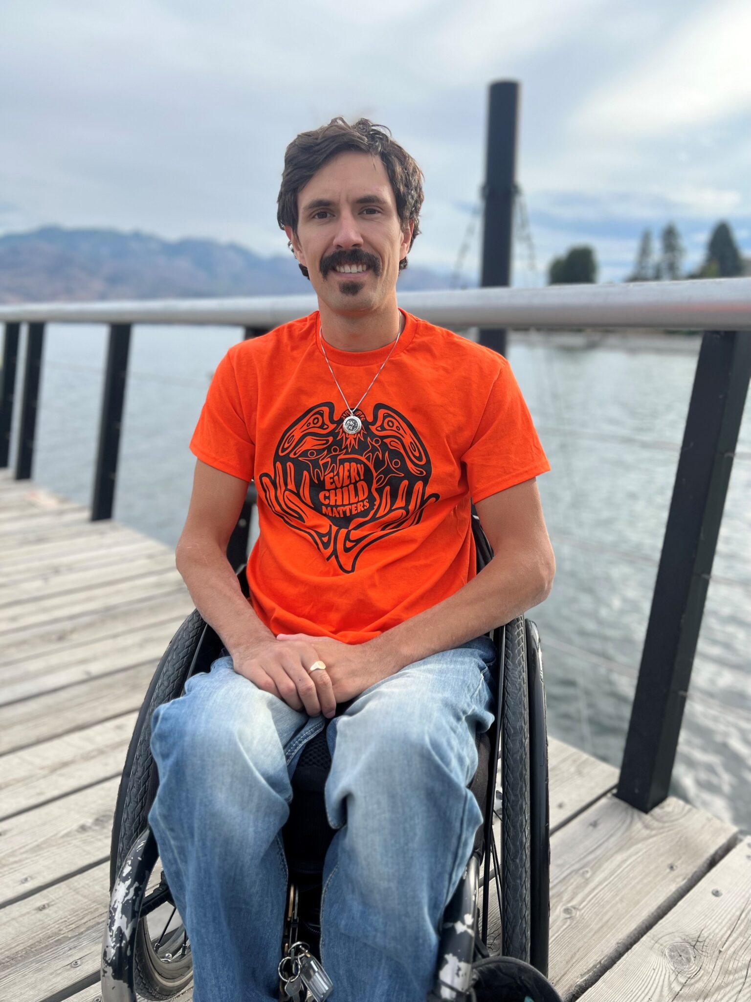 William, who is in a wheelchair, wears an orange shirt with text 