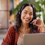 A woman wearing a headset uses a laptop.