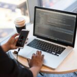 A woman goes on the phone while writing code on her laptop