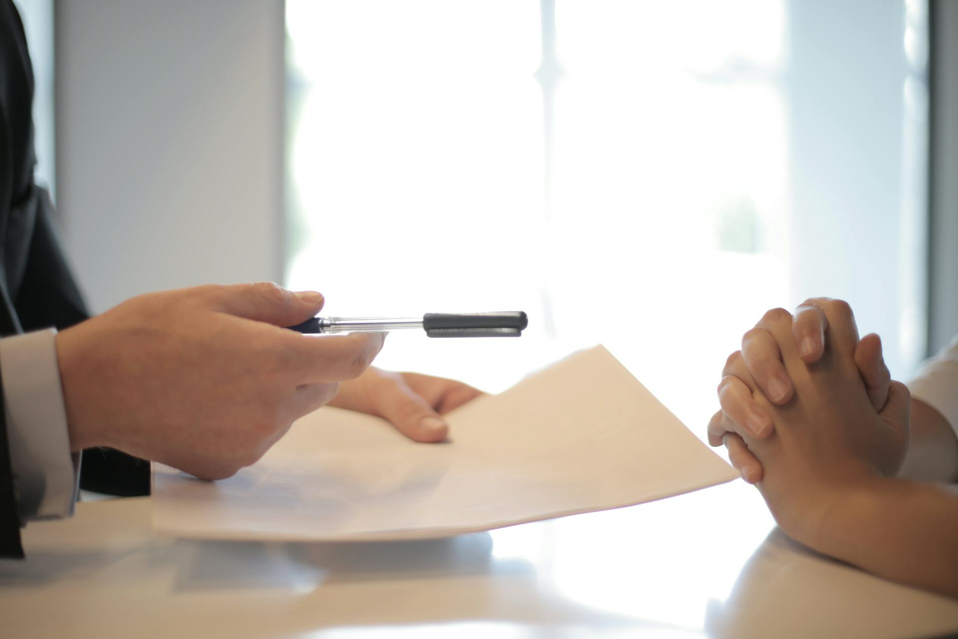 A man in a suit holding a pen and paper talks to a client.