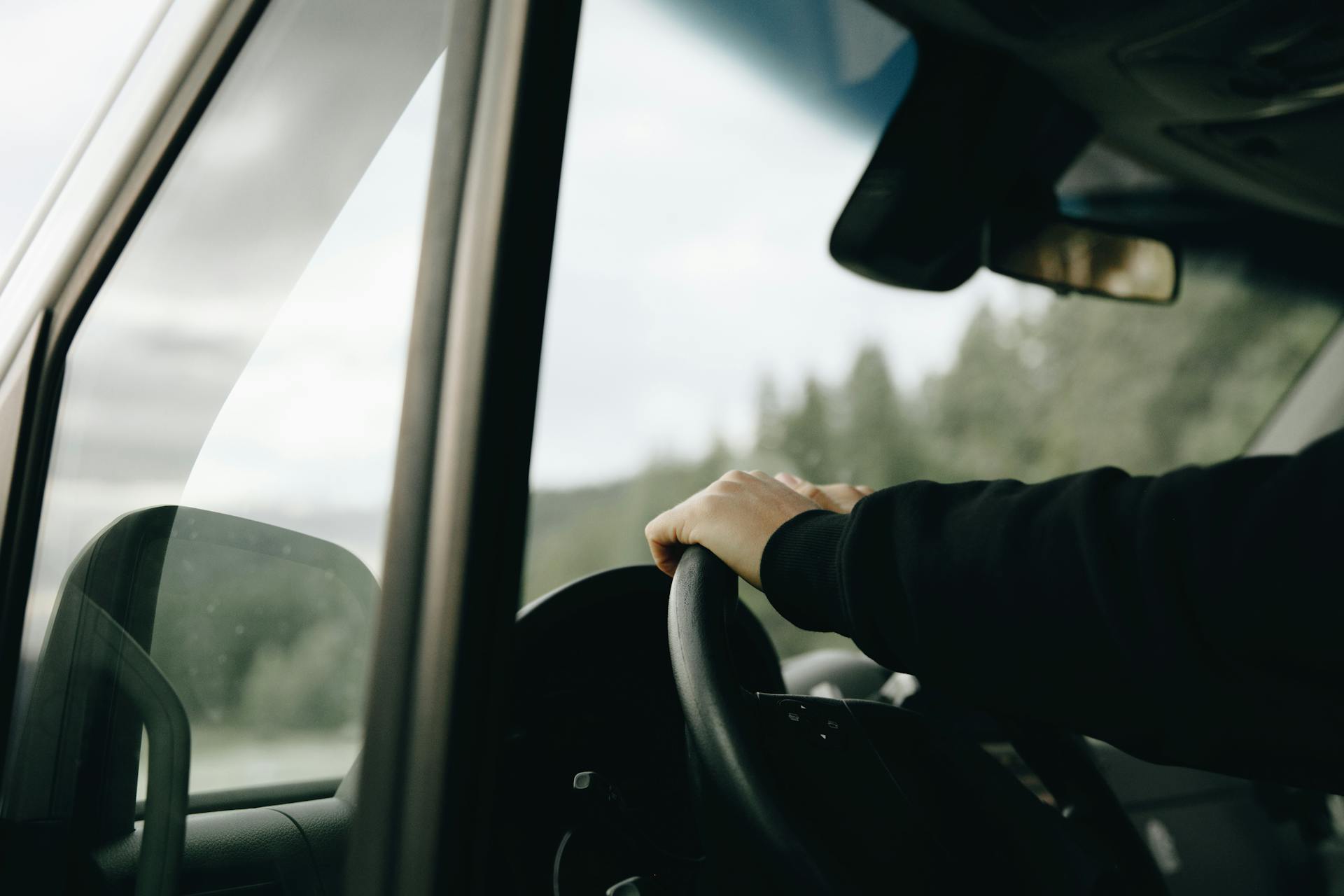 A person has their hand on the steering wheel as they drive.