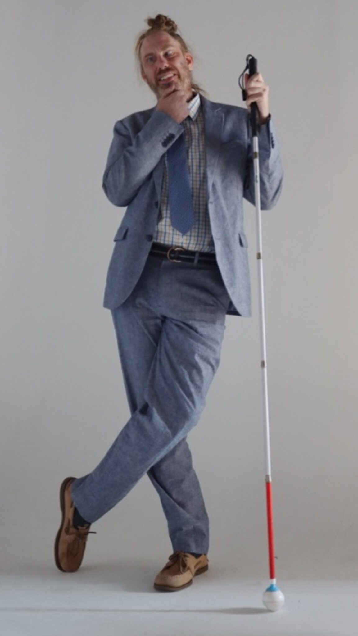 Dougie stands with his legs crossed, and has a thinking pose. He is wearing a suit and leaning on his white cane.